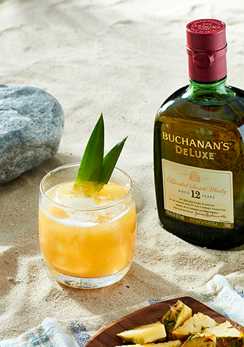A buchanita cocktail in a highball glass in front of a bottle of Buchanan's Deluxe