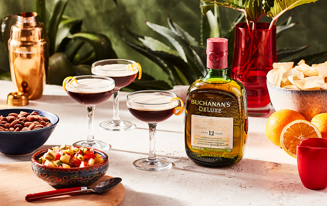 Two Bucatica cocktails sitting next to an empty coupe glass and a bottle of Buchanan's Deluxe