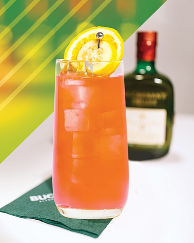 The Buchanan's La Familia cocktail garnished with a lemon slice. A bottle of Buchanan's Deluxe is blurred in the background. 
