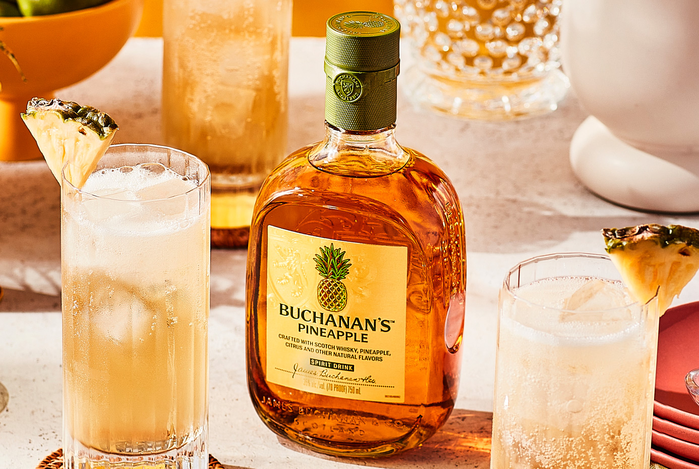 A bottle of Buchanan's Pineapple positioned between two Piña Fizz drinks on a counter