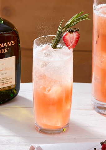 A person pouring the summer bonfire drink into a glass from a pitcher, next to a bottle of Buchanan's Deluxe
